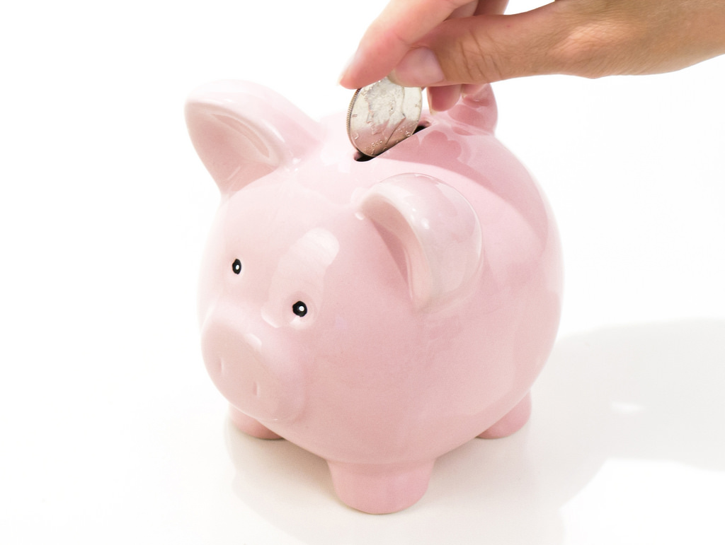 Hand putting coin into a pink piggy bank saving for RESP