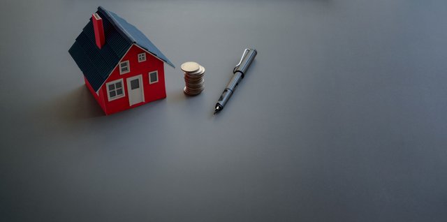 Small model of a red house with pile of coins and pen