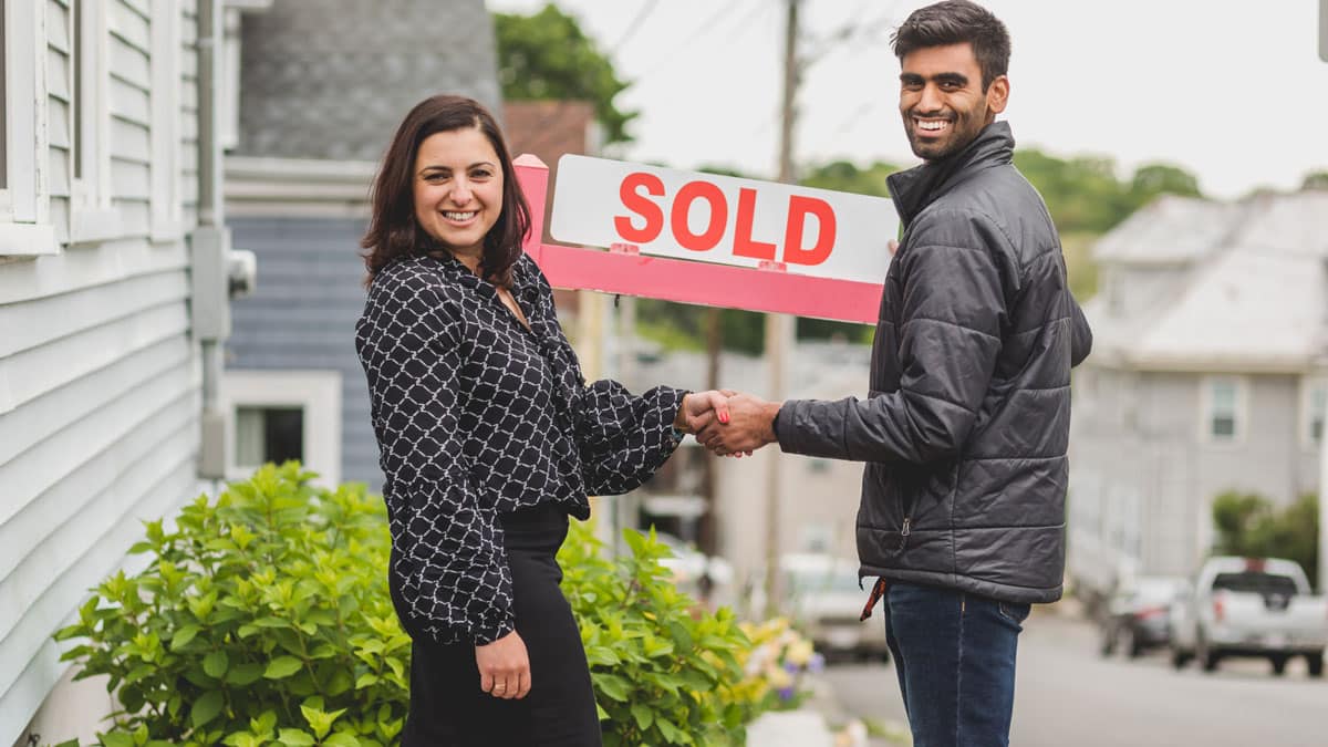 Couple standing in front of “SOLD” sign for their new home