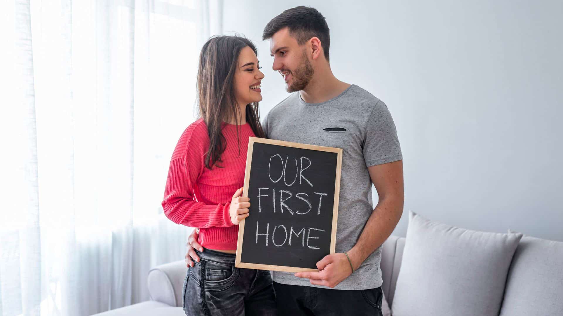 first time home buyers with a sign that says “our first home”